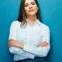 Smiling business woman with crossed arms portrait on blue wall. White shirt.